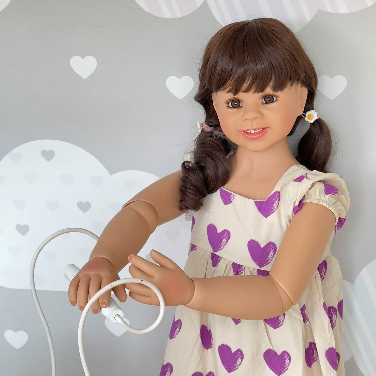 Muñeca Reborn de pie para niños pequeños, tamaño real (43 pulgadas), con cuerpo completo de vinilo; viste un vestido morado con estampado de corazones y mangas con volantes. 