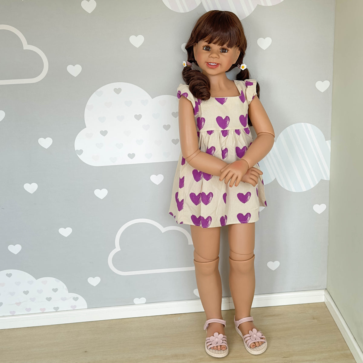 Muñeca Reborn de pie para niños pequeños, tamaño real (43 pulgadas), con cuerpo completo de vinilo; viste un vestido morado con estampado de corazones y mangas con volantes. 