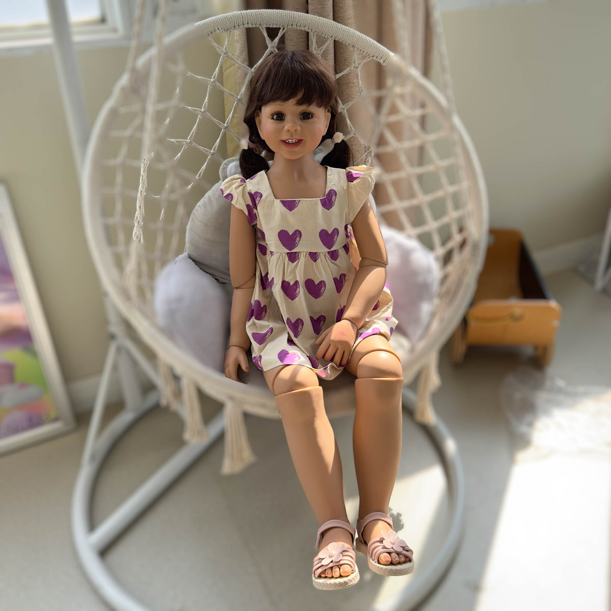 Muñeca Reborn de pie para niños pequeños, tamaño real (43 pulgadas), con cuerpo completo de vinilo; viste un vestido morado con estampado de corazones y mangas con volantes. 
